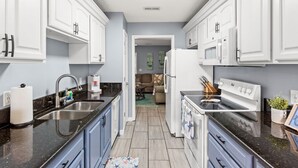 A modern kitchen with white cabinetry, a black countertop, stainless steel appliances, and a view into a living area.