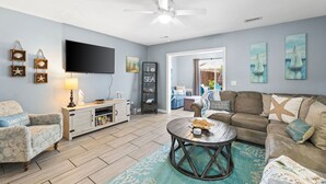 A living room with a flat-screen TV, a ceiling fan, a wooden cabinet, a sofa, and a coffee table.