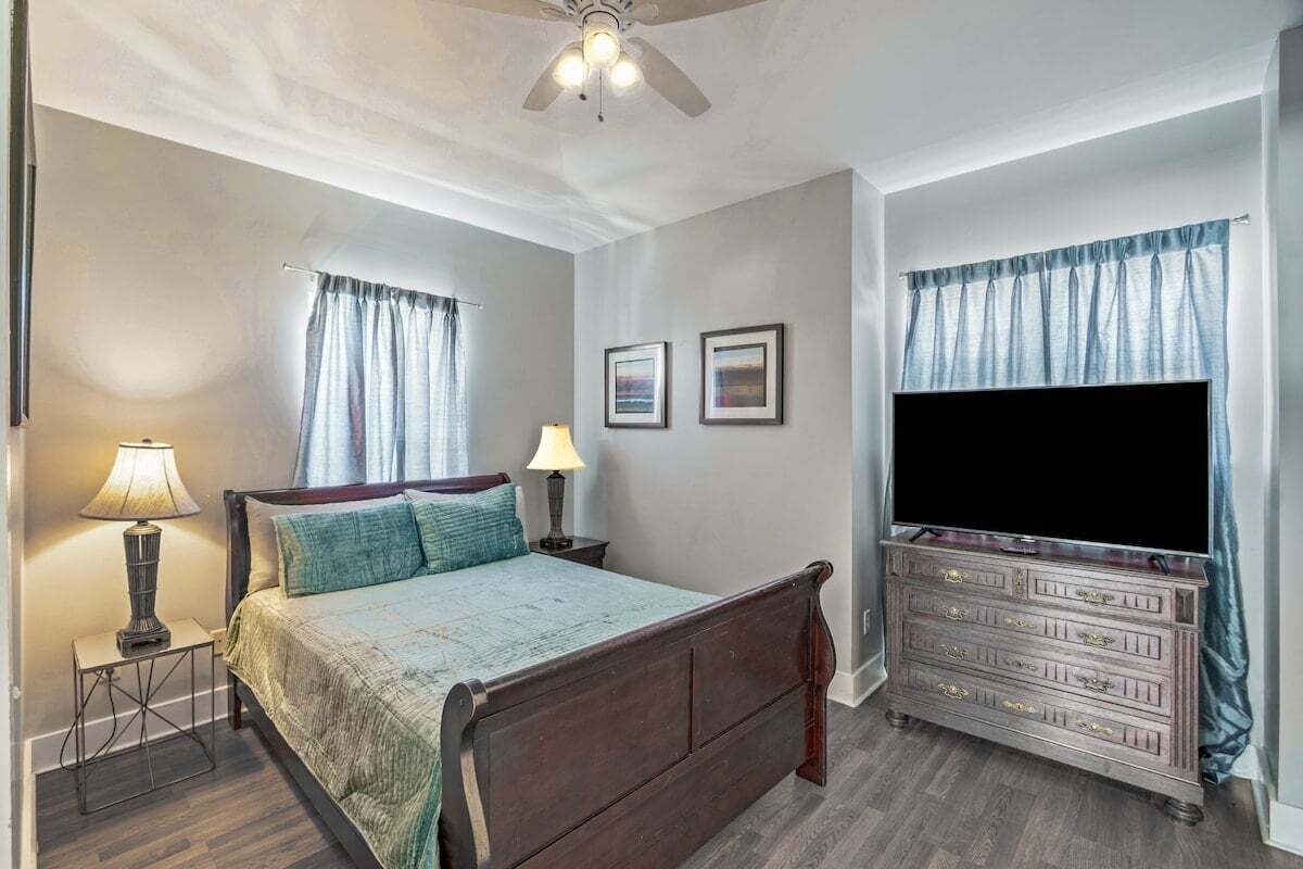 A bedroom with a bed, bedside lamps, a dresser, a flat-screen TV, and two framed pictures on the wall.