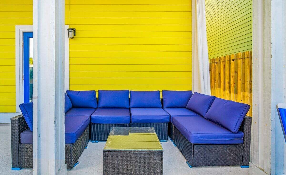 A bright yellow exterior wall with a blue outdoor seating area consisting of a sofa and a coffee table.