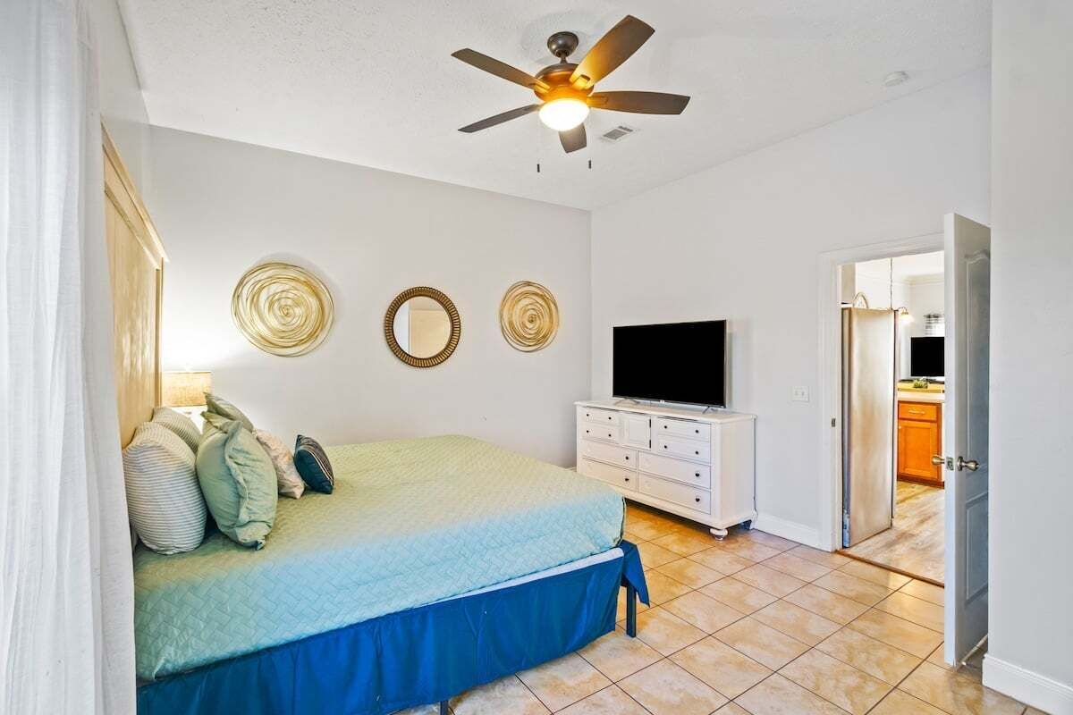 A bedroom with a bed, a ceiling fan, a TV, and a dresser.