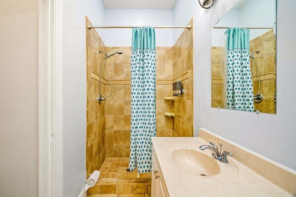 A bathroom with a beige sink, a mirror, and a shower with a blue and white polka dot shower curtain.