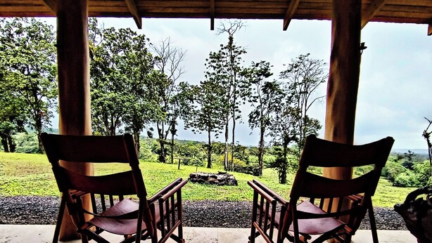 Deux fauteuils à bascule sont placés face à un paysage verdoyant, sous une pergola en bois.