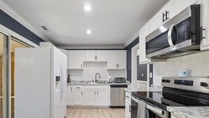 Une cuisine moderne avec des meubles blancs, un réfrigérateur en acier inoxydable, un four à micro-ondes, un four traditionnel et un lave-vaisselle.
