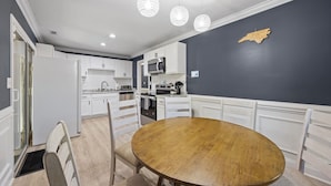 Une cuisine moderne avec des meubles blancs, une table de salle à manger ronde en bois et des luminaires suspendus.
