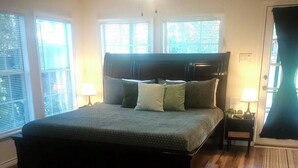A bedroom with a large bed, wooden flooring, and a ceiling fan.