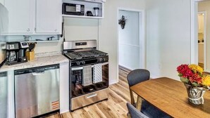 A modern kitchen with stainless steel appliances, a wooden dining table, and a vase of flowers.