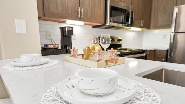 A kitchen with white marble countertops, a sink, and wooden cabinets.