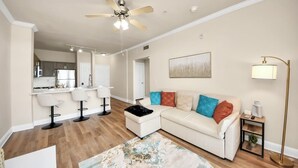 A modern living room with a white sofa, colorful cushions, a ceiling fan, and a floor lamp.
