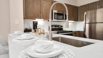 A modern kitchen with a white marble countertop, stainless steel appliances, and wooden cabinets.