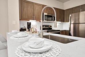 Une cuisine moderne dotée d’un plan de travail en marbre blanc, d’appareils électroménagers en acier inoxydable et d’armoires en bois.