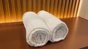 Two rolled white towels on a wooden table with a wooden slatted background. - Affordable Transient Room in Lipa City Near SM and LIMA (Lipa City)