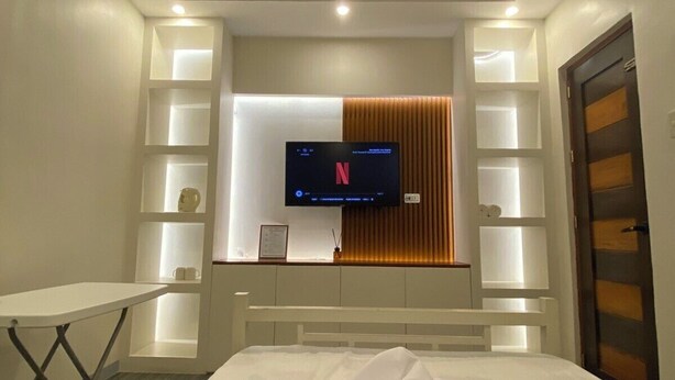 A hotel room with a bed, a TV mounted on the wall, and a desk with a lamp. - Affordable Transient Room in Lipa City Near SM and LIMA (Lipa City)