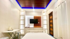 A hotel room with a bed, a desk, a chair, a television mounted on the wall, and a curtain on the window. - Affordable Transient Room in Lipa City Near SM and LIMA (Lipa City)