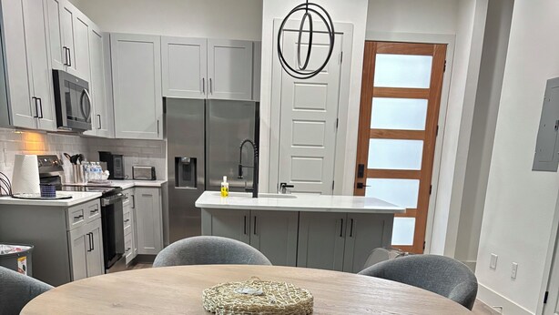 Una cocina moderna con armarios grises, una isla central y una mesa de comedor redonda con sillas tapizadas en gris.