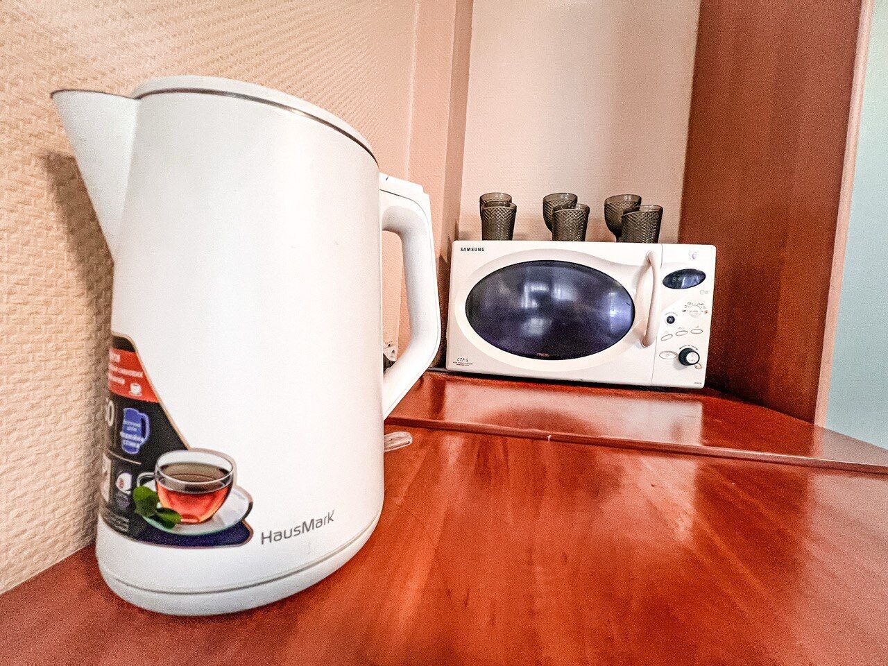 Una tetera blanca con diseño de taza de té y un microondas sobre una superficie de madera.