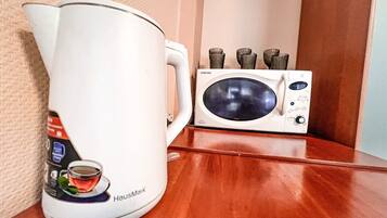 Una tetera blanca con diseño de taza de té y un microondas sobre una superficie de madera.
