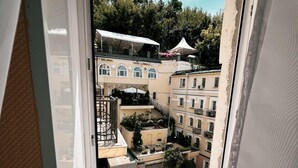 Una ventana con vistas a un patio con edificios, una sombrilla blanca y vegetación.