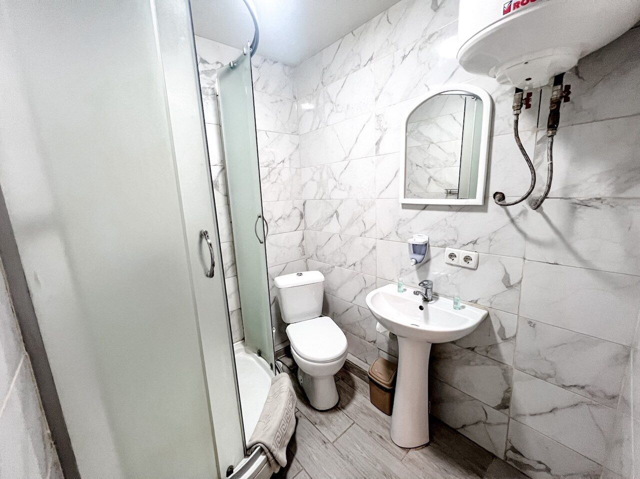 A bathroom with a glass shower enclosure, a toilet, and a pedestal sink.