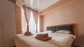 Una habitación de hotel con una cama grande, cabecera y ventana con cortinas.