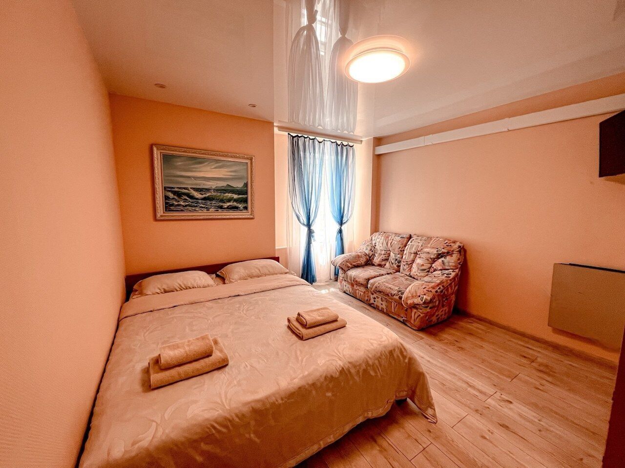 Un dormitorio con una cama grande, una silla, un cuadro en la pared y una ventana con cortinas.