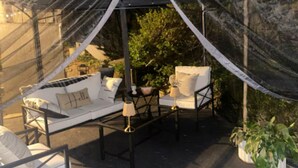 A tented outdoor seating area with a sofa and chairs, a small table, and potted plants. - Peaceful Pines Haven~ cozy studio near the ponds (Hanson)