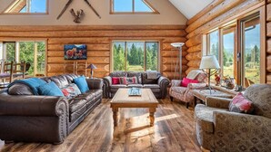 A log cabin interior with a large sofa, a patterned armchair, and a coffee table.