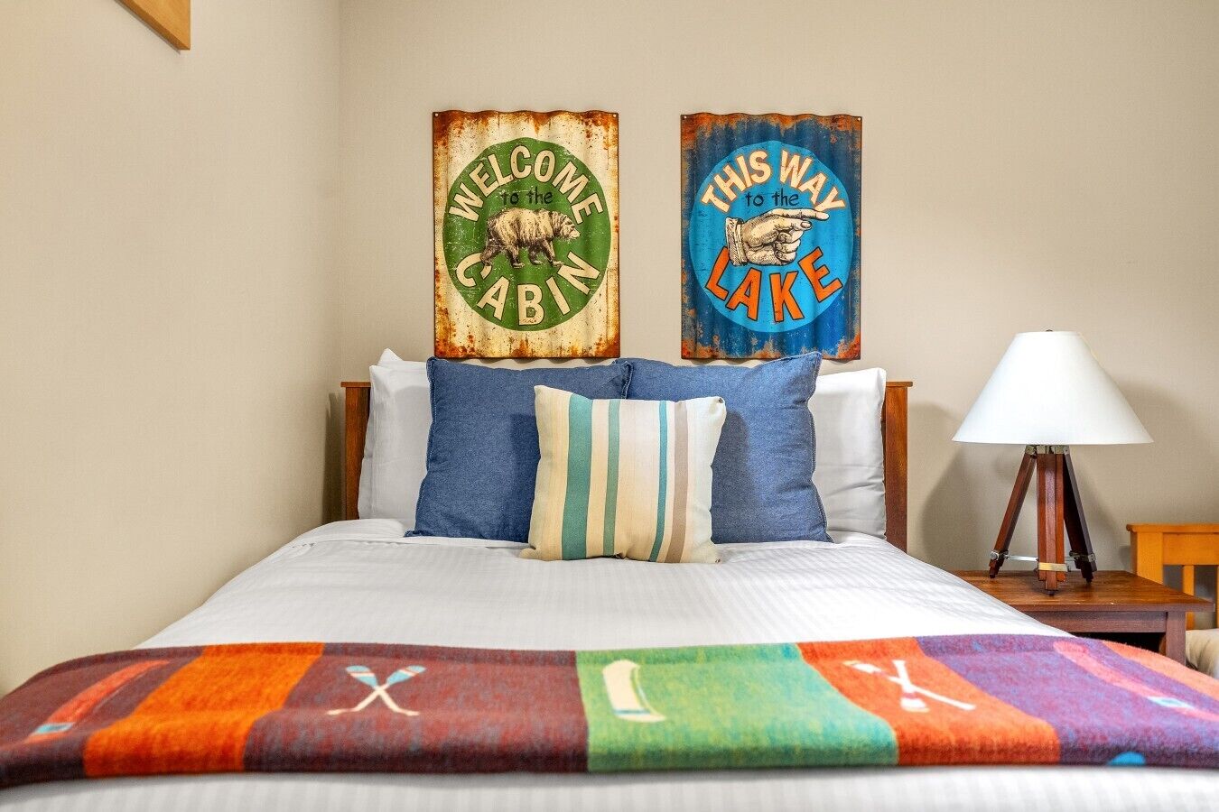 Un lit avec une couverture colorée, deux oreillers et deux éléments de décoration rustiques accrochés au mur.