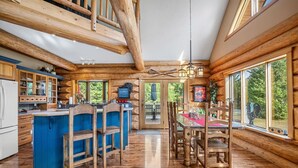 A log cabin interior with a kitchen, dining area, and large windows.