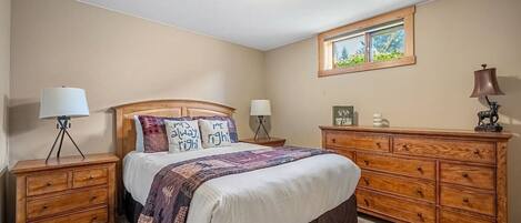 A bedroom with a bed, two nightstands, a dresser, and a window.