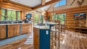 A spacious log cabin kitchen with a central island, large windows, and a dining area.