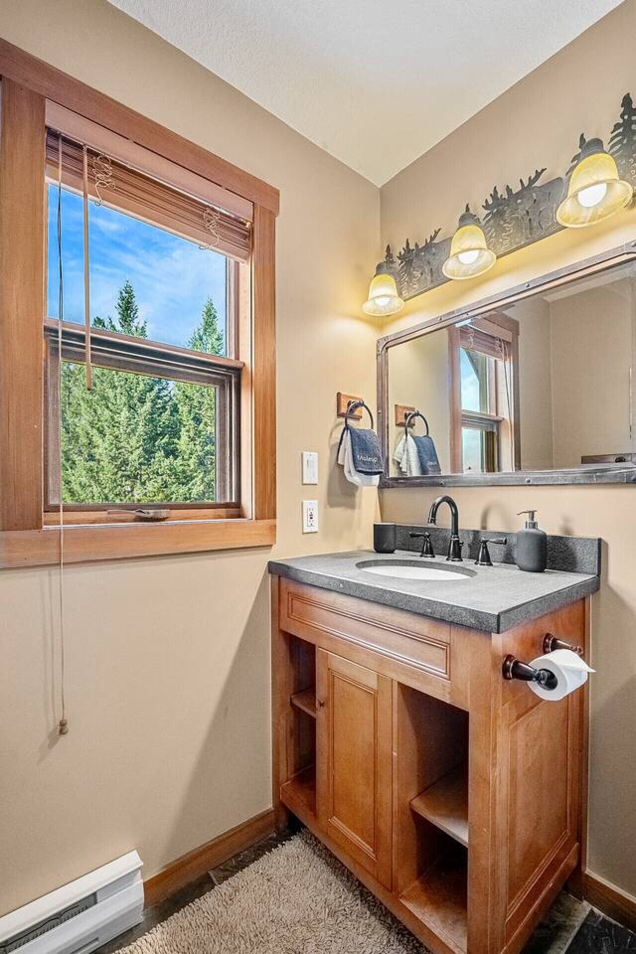 A bathroom with a wooden vanity, a large mirror, and a window with a view of trees.