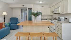 A modern kitchen with white cabinets, a wooden island, and a blue chair. - Two Suns at The Beach - White Sand and Shopping (Orange Beach)