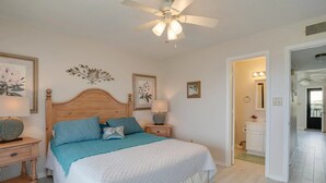 A bedroom with a wooden headboard, a large bed with blue and white bedding, a nightstand with a lamp, and a ceiling fan. - Two Suns at The Beach - White Sand and Shopping (Orange Beach)