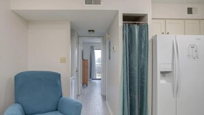 A narrow hallway with a blue armchair, a white refrigerator, and a teal curtain. - Two Suns at The Beach - White Sand and Shopping (Orange Beach)