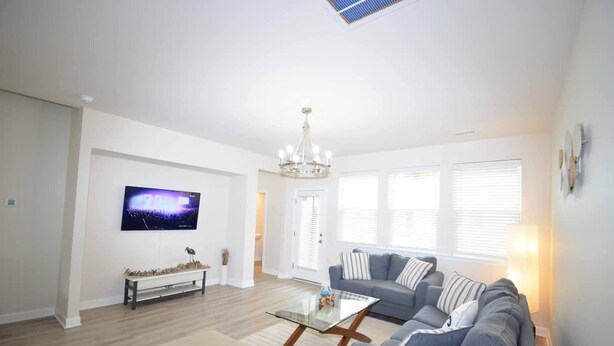 A modern living room with a flat-screen TV, a glass coffee table, a grey sofa, and a bench.
