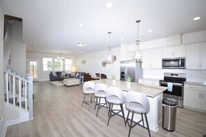 A modern kitchen with white cabinets, stainless steel appliances, and a central island with bar stools. - Getaway on Mclernon - Top Notch Mid Term Stay (Johns Island)