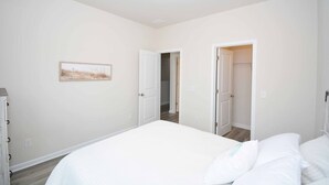 A bedroom with a large bed, a dresser, and a door leading to another room.