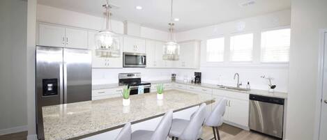 A modern kitchen with white cabinetry, stainless steel appliances, a granite countertop, and bar stools.