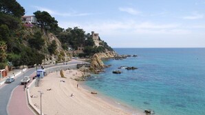 A coastal beach with a castle on a cliff, a paved walkway, and clear blue waters. - Rosamar Maxim Adults Only (Lloret de Mar)