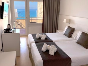 Een hotelkamer met twee bedden, een bureau en uitzicht op zee.