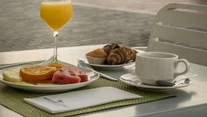 A table with breakfast items including croissants, a glass of orange juice, and a cup of coffee, set against a scenic coastal backdrop with a castle. - Rosamar Maxim Adults Only (Lloret de Mar)