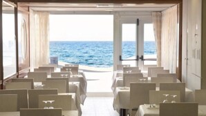 A dining area with tables and chairs, a view of the ocean through a doorway, and a tiled floor. - Rosamar Maxim Adults Only (Lloret de Mar)