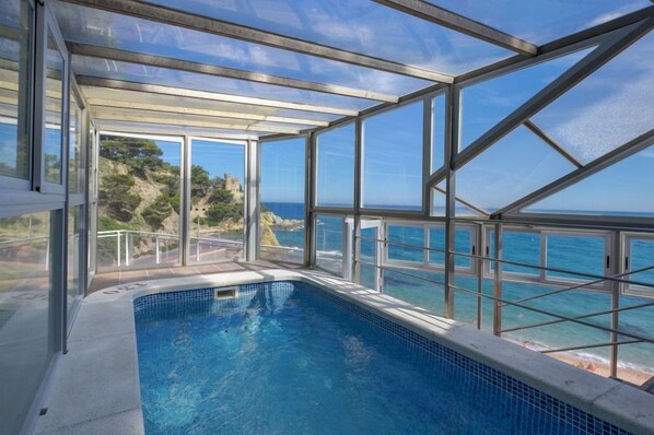 Una piscina cubierta por cristal con vista clara al océano y un castillo lejano.