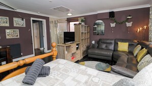 Sala de estar com sofá, televisão, armário de madeira e cama com colcha estampada.