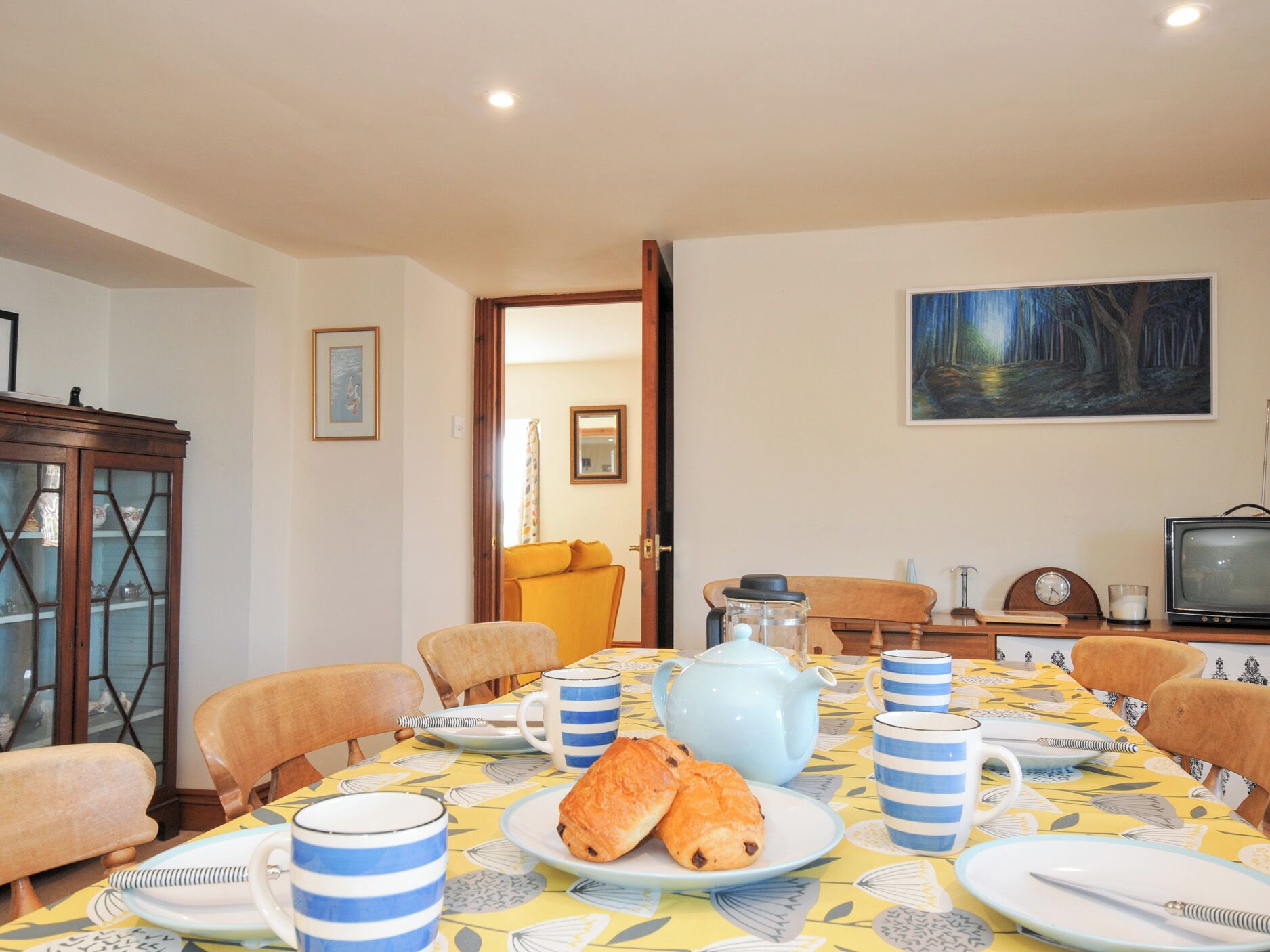 A dining area with a table set for breakfast, including croissants and coffee cups.