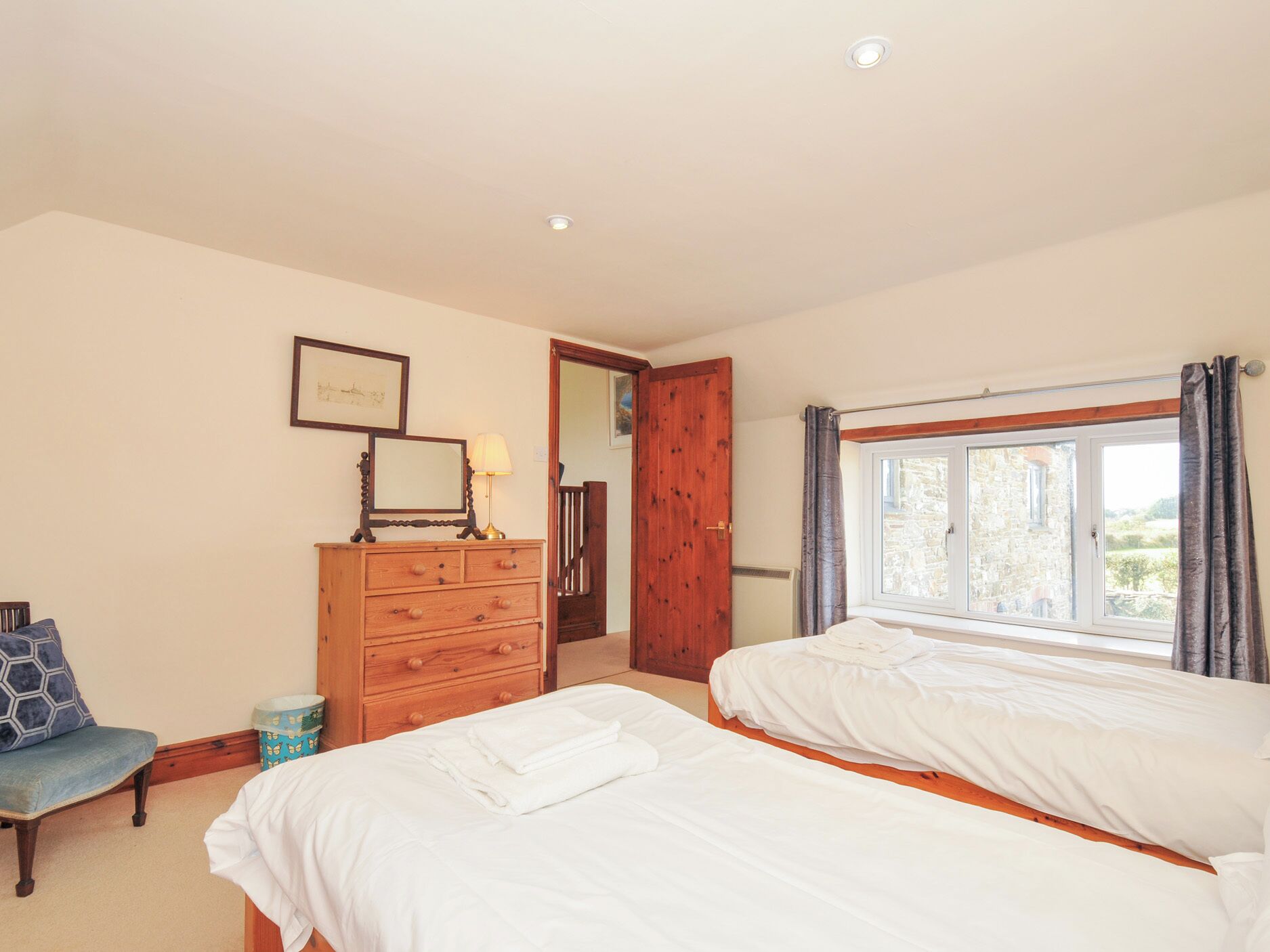 Een slaapkamer met twee bedden, een houten dressoir, een spiegel en een raam met gordijnen.
