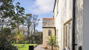 A house with a stone wall, a wooden gate, and a garden with various plants. - Rosewin Farmhouse (Wadebridge)