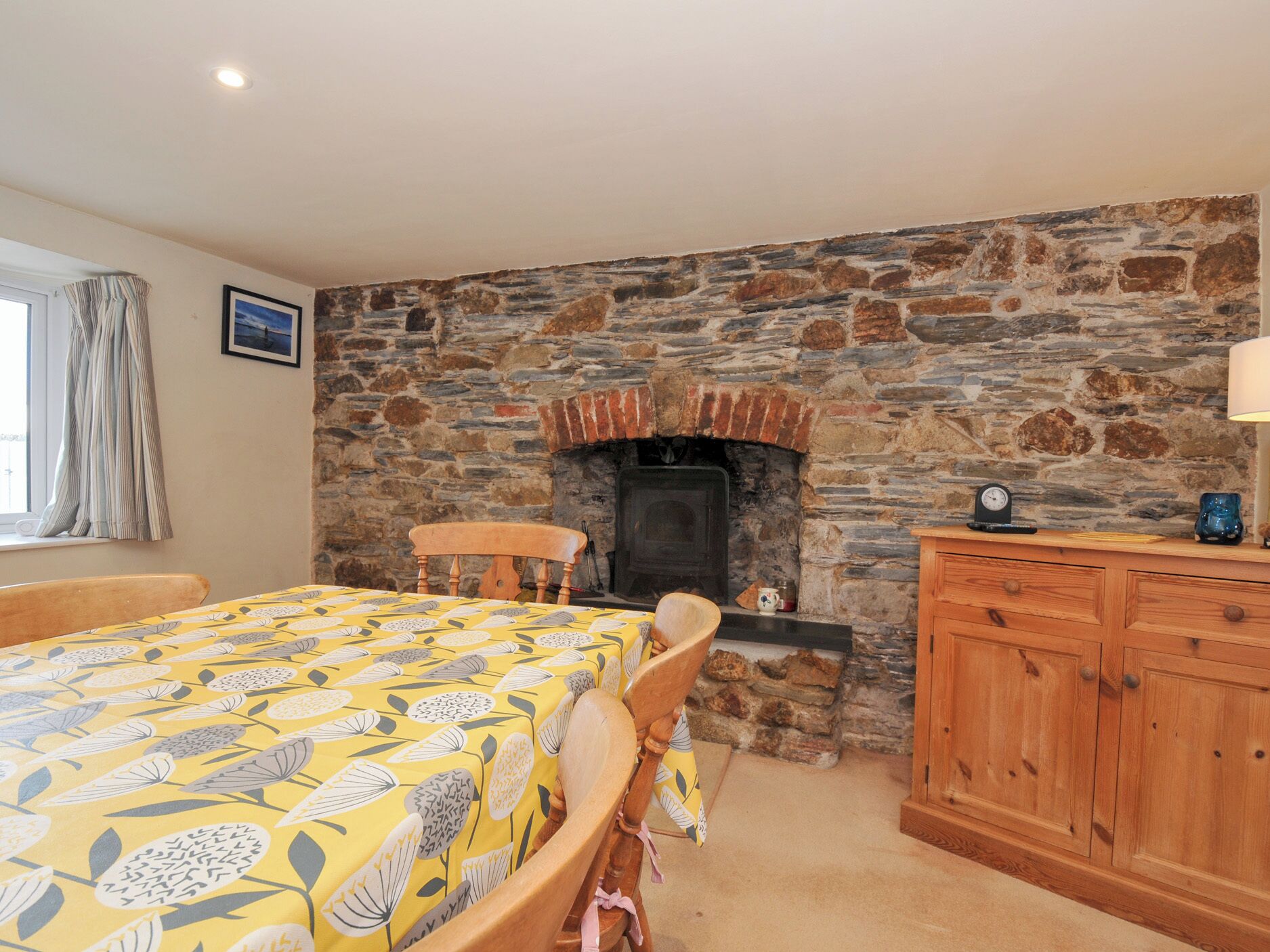 A room with a stone wall, a fireplace, a bed with a floral bedspread, a wooden chair, and a wooden cabinet.