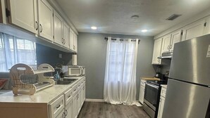 A kitchen with white cabinets, a stainless steel refrigerator, a microwave, and a wooden countertop.
